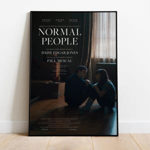 May include: A framed poster for "Normal People" with Daisy Edgar-Jones and Paul Mescal. The poster has a black frame and the title in white. The image shows two people sitting on the floor, with text at the top and bottom.