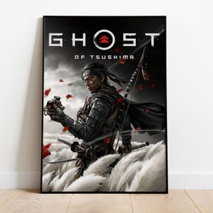 May include: A framed poster featuring the game "Ghost of Tsushima." The artwork depicts a samurai warrior in armor, holding a weapon, with a bow and arrow. The background is a mix of white, red, and gray tones, with the game's title at the top.