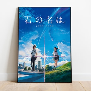Puede incluir: Un póster enmarcado con ilustraciones de anime. La imagen muestra dos personajes frente a un cielo azul brillante con nubes y un paisaje urbano. Texto japonés y la frase en inglés "your name" se muestran en la parte superior.