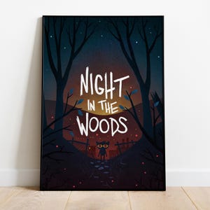 May include: A framed art print depicting a night scene in a forest. The artwork features the text "NIGHT IN THE WOODS" in white, above a silhouetted figure with glowing eyes. The background shows trees, a fence, and a starry sky.