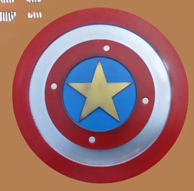 K&ouml;nnte beinhalten: Ein runder Schild mit einem roten Au&szlig;enring, einem silbernen Mittelring und einem blauen Zentrum. Ein goldener Stern befindet sich in der Mitte des blauen Kreises. Der Schild hat drei wei&szlig;e Nieten und ist eine Superhelden-Replik.