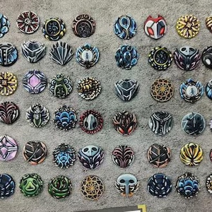 May include: A collection of intricately designed, circular decorative objects. Each piece features unique patterns and color combinations, including shades of blue, red, gold, and black. The objects are arranged on a textured, gray surface.
