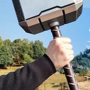 K&ouml;nnte beinhalten: Ein silberner und brauner Requisitenhammer mit aufwendigen Details. Der Hammer hat einen rechteckigen Kopf mit dekorativen Mustern und einen braunen Griff. Der Griff ist mit einem strukturierten Material umwickelt. Am Boden ist eine Lederschlaufe befestigt.