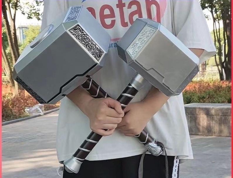 K&ouml;nnte beinhalten: Zwei silberne und schwarze Spielzeugh&auml;mmer mit aufwendigen Designs auf den K&ouml;pfen und dunkelbraunen Griffen. Die H&auml;mmer werden vor einer Person gehalten, die ein wei&szlig;es T-Shirt tr&auml;gt. Die H&auml;mmer scheinen Nachbildungen einer fiktiven Waffe zu sein.