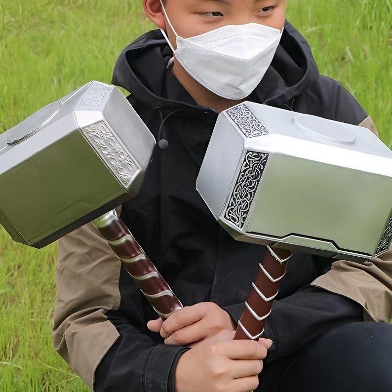 K&ouml;nnte beinhalten: Zwei silberne Spielzeugh&auml;mmer mit braunen Griffen. Die Hammerk&ouml;pfe haben dekorative silberne Muster. Die Griffe sind mit einem braunen Material mit silbernen Akzenten umwickelt. Eine Person mit einer schwarzen Jacke h&auml;lt die H&auml;mmer.