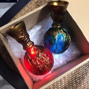 May include: Two decorative glass bottles with ornate gold-colored tops and glowing bases. One bottle glows red, the other blue and green. They are inside a cardboard box with bubble wrap.