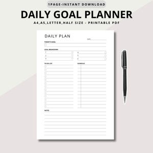 Peut inclure: Un planificateur quotidien blanc avec le texte "DAILY GOAL PLANNER" en haut. Le planificateur comprend des sections pour les plans quotidiens, les objectifs et les listes de tâches. Un stylo noir est placé à côté du planificateur.