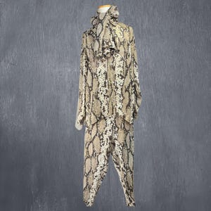 May include: A two-piece snakeskin print outfit, consisting of a long-sleeved top with a hood and matching pants. The outfit is displayed on a mannequin against a gray background. The print features shades of brown, tan, and cream.