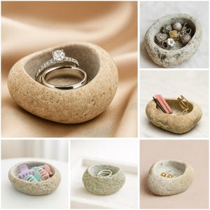 May include: A collection of small, natural stone bowls. One bowl holds a diamond engagement ring and a wedding band. Other bowls contain jewelry, hair accessories, and earrings. The bowls are various shades of gray and beige, with a rough, textured surface.