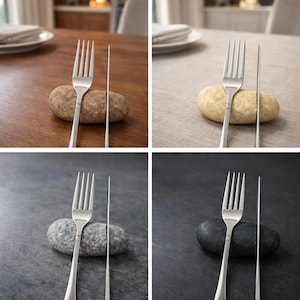 May include: A stainless steel fork and knife set displayed with a smooth, oval stone. The fork has four tines, and the knife has a long, slender blade. The set is presented on a dark surface, creating a minimalist aesthetic.