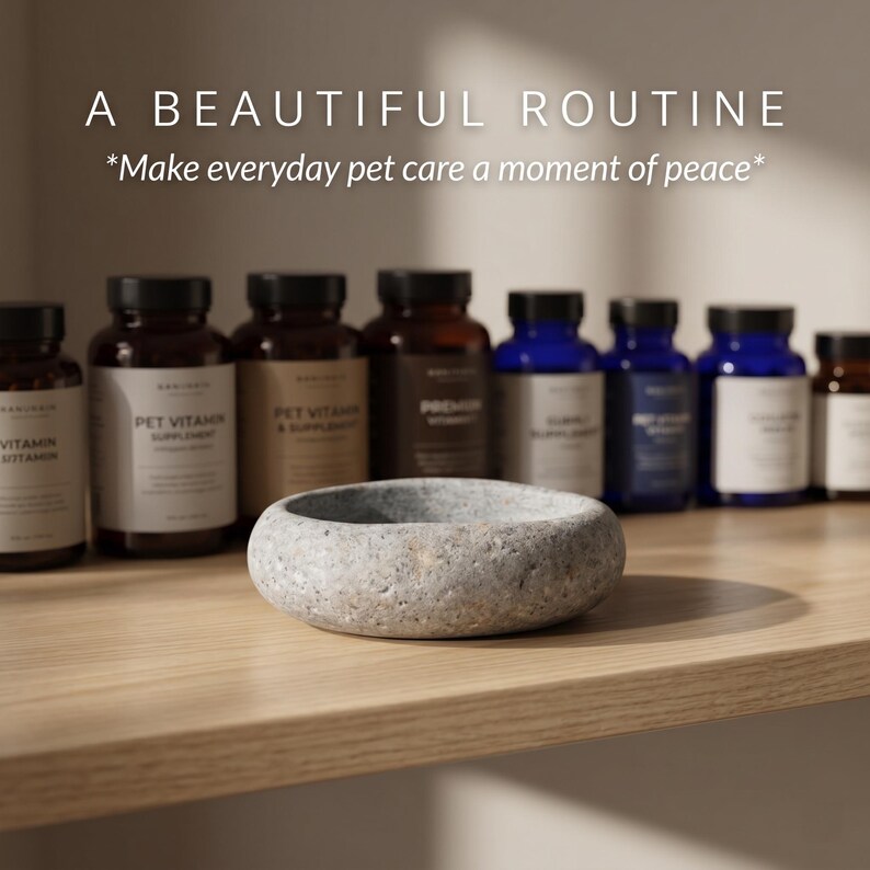 Puede incluir: Un cuenco de piedra gris para mascotas sobre una estanter&iacute;a de madera, frente a varias botellas de suplementos. Las botellas son marrones y azules con etiquetas blancas. El texto en la parte superior dice "A BEAUTIFUL ROUTINE" y "*Make everyday pet care a moment of peace*."