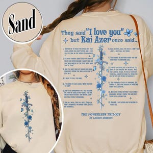 May include: Sand-colored sweatshirt with text and a floral and sword design. The back of the shirt features the quote "They said 'I love you' but Kai Azer once said..." and a list of quotes. The front has a sword and floral design.