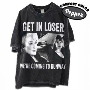 Könnte beinhalten: Pfefferfarbenes T-Shirt mit dem Text "GET IN LOSER" über einem Schwarz-Weiß-Bild von zwei Frauen. Unter dem Bild steht der Text "WE'RE COMING TO RUNWAY". Ein Comfort Color-Logo befindet sich oben rechts.