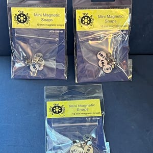May include: Three clear plastic hanging bags containing silver-colored 10 mm mini magnetic snaps. Each bag features a yellow label with the text 'the Around Bobbin', 'Mini Magnetic Snaps', '10 mm magnetic snaps', and the code 'ATB-199-HK'.