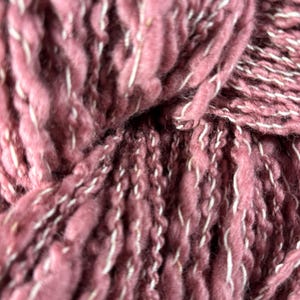 May include: Close-up of a skein of dusty rose-colored yarn with white flecks. The thick, textured yarn is tightly wound, showcasing its chunky, irregular strands. Ideal for knitting or crocheting projects.