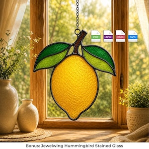 May include: A stained glass suncatcher shaped like a yellow lemon with two textured green leaves, outlined in black metal cames. The piece hangs from a metal chain and features a vibrant, translucent yellow body with a pebbled glass surface texture.