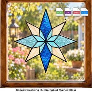 May include: A star-shaped stained glass suncatcher featuring a geometric pattern with deep blue, light blue, and cream-coloured textured glass panels held together by dark metal framing, suspended by a thin metal chain in a window frame.