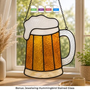 Può includere: Un acchiappasole in vetro colorato a forma di boccale di birra con una parte superiore in schiuma bianca e un corpo color ambra, delineato da profili in metallo nero. L'oggetto presenta un manico robusto ed è appeso a una catena in metallo nero.