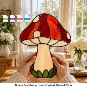 Può includere: Un acchiappasole in vetro colorato a forma di fungo con cappello rosso a macchie color crema, gambo color crema e foglie verdi alla base. L'oggetto è realizzato con linee di saldatura in metallo scuro e include icone di file PDF, JPG, PNG e SVG.