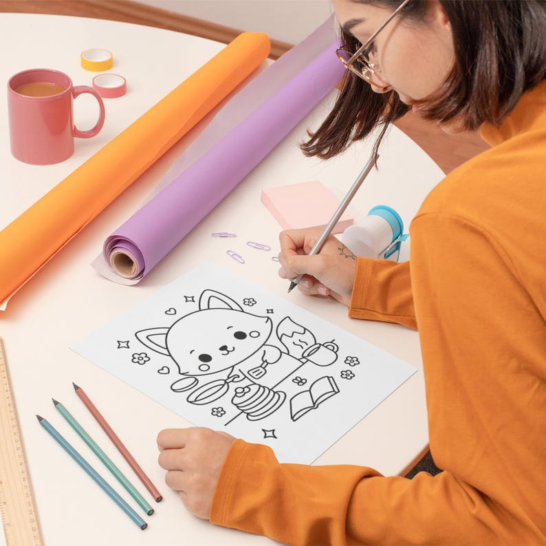 May include: A person drawing a coloring page of a cartoon fox cooking pancakes. The scene includes colored pencils, rolls of orange and purple paper, a pink mug, and tape. The person is wearing an orange long-sleeved shirt.