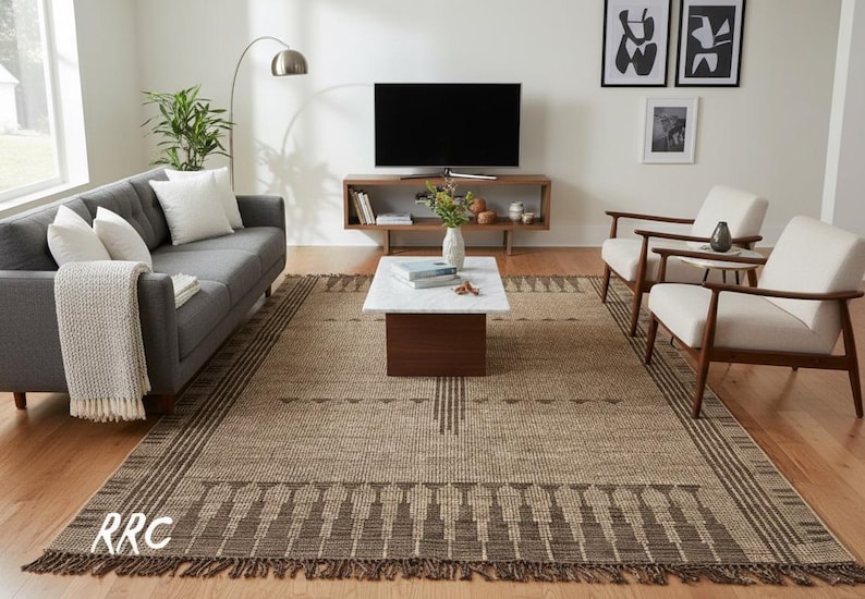 May include: A neutral-toned area rug with a geometric pattern and fringe. The rug is in a living room setting with a gray sofa, white chairs, and a wooden coffee table. The rug's dimensions are approximately 8 x 10 feet.