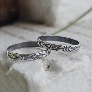 May include: Two silver rings featuring a repeating embossed floral pattern with oxidized detailing. The bands have a polished finish on the raised flower motifs and a darkened, recessed background, creating a distinct contrast across the metal surface.