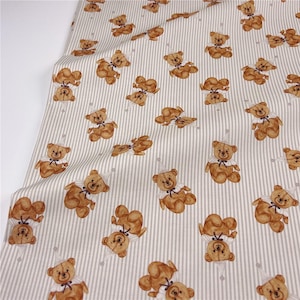 Op de afbeelding: Stof met een herhaald patroon van bruine teddyberen met feesthoeden en vlinderdassen, tegen een achtergrond van verticale grijze en witte strepen. De beren staan in verschillende poses, wat een speels ontwerp creëert.