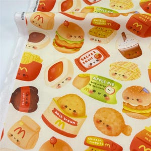 May include: A white fabric featuring a repeating pattern of cartoon fast food items with smiling faces, including hamburgers, chicken nuggets, french fries, apple pies, hash browns, and a drink cup, all decorated with red and yellow accents.