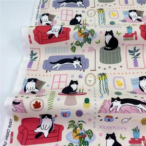 Può includere: Un tessuto in cotone color crema con un motivo ripetuto di gatti tuxedo bianchi e neri in varie pose, tra cui seduti su divani rossi, sdraiati su divani viola e a riposo su tappeti, intervallati da piante in vaso e piccoli giocattoli.