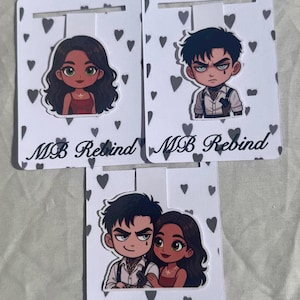 Puede incluir: Tres tarjetas blancas para exhibición de pendientes con ilustraciones de personajes de dibujos animados. Cada tarjeta tiene una ilustración de personaje diferente. Las tarjetas están decoradas con formas de corazón grises y el texto "MB Rebind".
