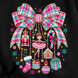 May include: A black long-sleeve sweatshirt featuring a large, colorful graphic of a pink and teal plaid bow. Hanging from the bow are illustrations of a nutcracker, a ballerina, a candy cane, a gingerbread house, a stocking, a drum, and a gift.