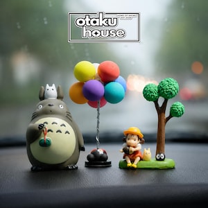 May include: A set of three decorative figurines featuring a large grey creature with a small white figure on its head, a cluster of colourful balloons on a silver wire stand, and a small figure sitting under a tree with a tiny black creature.