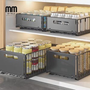 Puede incluir: Un sistema de organización de despensa de cocina con cestas extraíbles de metal gris oscuro. Las cestas están llenas de varios frascos y recipientes, incluidos frascos de vidrio con contenido amarillo y rojo, y tapas de madera.