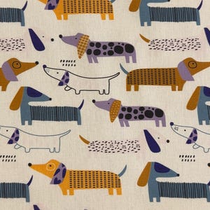 Könnte beinhalten: Ein hellbeiger Stoff mit einem sich wiederholenden Muster aus stilisierten Dackeln in verschiedenen Farben wie Braun, Blau, Violett und Weiß. Die Hunde sind mit unterschiedlichen Texturen wie Streifen und Punkten dargestellt, durchsetzt mit kleinen schwarzen Strichen.