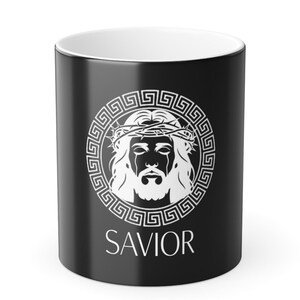 May include: Black ceramic mug with a white interior. The mug features a white graphic of a face with a crown of thorns, surrounded by a Greek key design. The word "SAVIOR" is printed below the graphic.
