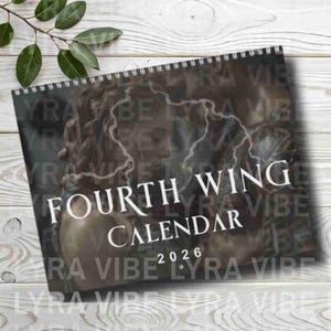 May include: A spiral-bound calendar with the text "FOURTH WING CALENDAR 2026" in white. The cover features a blurred image of a person with a lightning bolt design. The calendar is set against a light wood grain background.