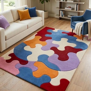 Könnte beinhalten: Ein farbenfroher Teppich mit einem Puzzleteil-Design. Der Teppich weist eine Mischung aus Farben auf, darunter Rot, Blau, Orange, Lila und Creme. Der rechteckige Teppich liegt auf einem Holzboden, mit einem Sofa und einem Stuhl im Hintergrund.