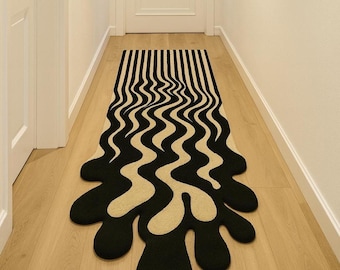 Pode incluir: Um tapete preto e bege com um design único e ondulado. O tapete apresenta listras verticais pretas que se transformam em uma forma orgânica e fluida. O tapete está colocado em um corredor com paredes claras e piso de madeira.