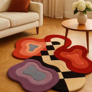 Könnte beinhalten: Ein Teppich mit unregelmäßiger, organischer Form und getufteter Textur. Das Design zeigt geschichtete, wellenförmige Farbblöcke in Rot, Orange, Violett und Hellblau, die von einem schwarz-cremefarbenen Schachbrettmuster durchzogen sind.