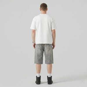 May include: A person wearing a white t-shirt, gray denim shorts with paint splatter, and black boots. The shorts have a raw hem. The person is facing away from the camera.