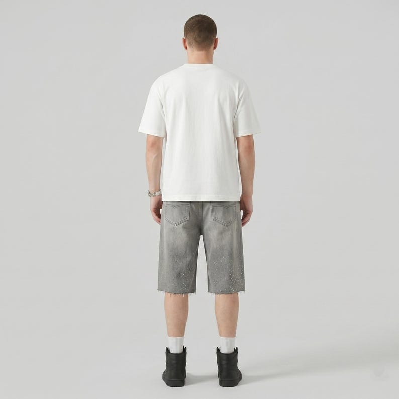 May include: A person wearing a white t-shirt, gray denim shorts with paint splatter, and black boots. The shorts have a raw hem. The person is facing away from the camera.