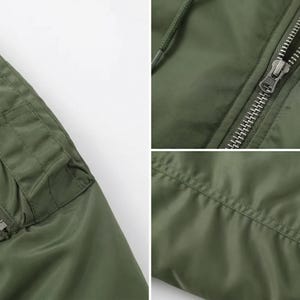 K&ouml;nnte beinhalten: Nahaufnahme einer olivgr&uuml;nen Bomberjacke. Details sind eine Rei&szlig;verschlusstasche, ein Metallrei&szlig;verschluss und gerippte B&uuml;ndchen. Die Jacke hat ein glattes, mattes Finish und ein klassisches Design.