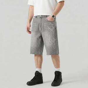 May include: Gray denim shorts with a raw hem and a faded design. The shorts feature white script on the side and small embellishments along the bottom hem. The shorts are worn with black high-top sneakers.