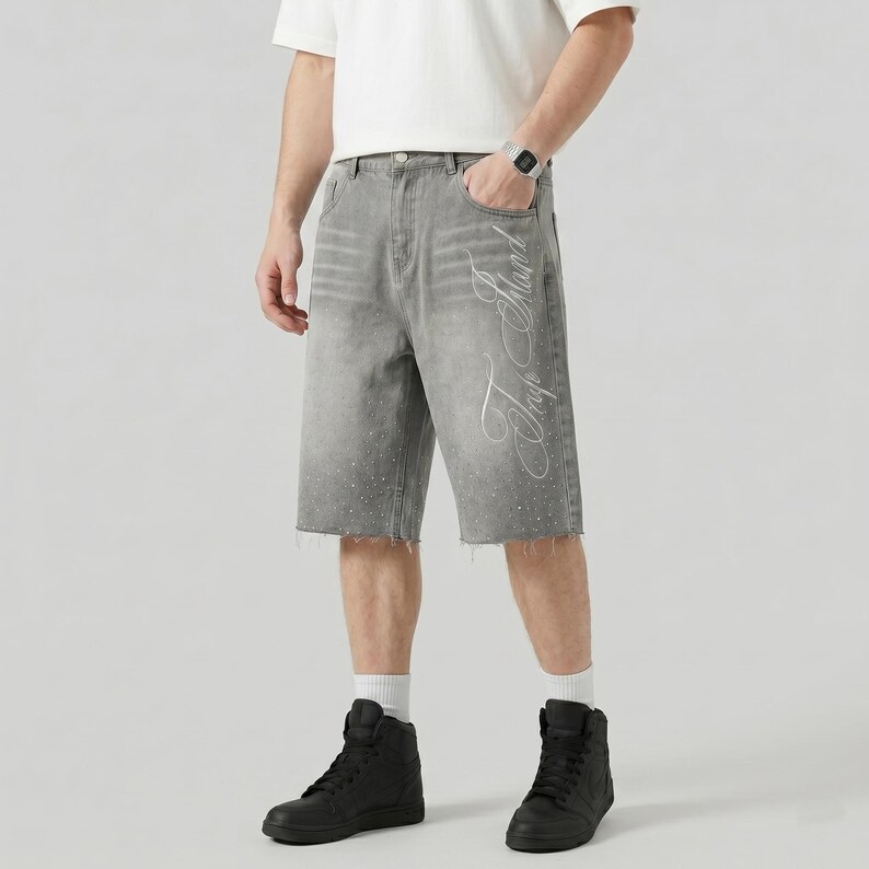 May include: Gray denim shorts with a raw hem and a faded design. The shorts feature white script on the side and small embellishments along the bottom hem. The shorts are worn with black high-top sneakers.