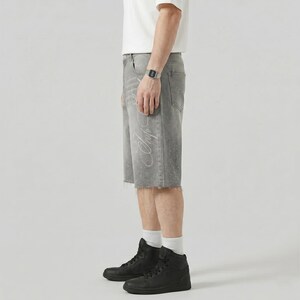 May include: Gray denim shorts with a raw hem and a white script design on the side. The shorts have a faded appearance and are paired with black high-top sneakers.