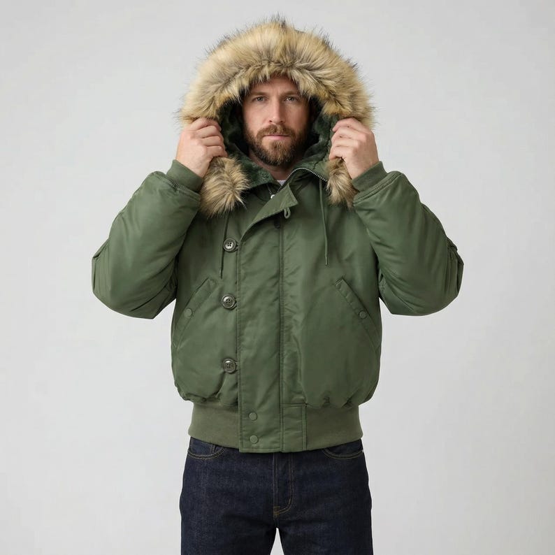 K&ouml;nnte beinhalten: Olivgr&uuml;ne Bomberjacke mit Kapuze mit Kunstfellfutter. Die Jacke hat eine Knopfleiste, gerippte B&uuml;ndchen und einen gerippten Saum. Das Model tr&auml;gt eine dunkelblaue Jeans. Ein klassisches Oberbekleidungsst&uuml;ck.