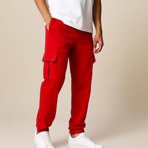 Puede incluir: Pantalones cargo de color rojo brillante con dos bolsillos grandes en la pierna izquierda. Los pantalones están hechos de un material suave y se combinan con zapatillas blancas y una camiseta blanca. El ajuste es relajado.