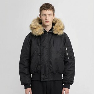 K&ouml;nnte beinhalten: Schwarze Bomberjacke mit Kapuze mit Kunstfellfutter. Die Jacke hat eine Rei&szlig;verschlusstasche am linken &Auml;rmel, einen gerippten Saum und Knopfverschl&uuml;sse. Der Kunstfellbesatz ist hellbraun.