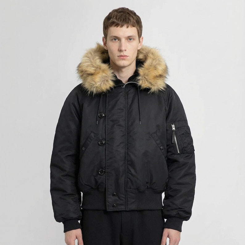 K&ouml;nnte beinhalten: Schwarze Bomberjacke mit Kapuze mit Kunstfellfutter. Die Jacke hat eine Rei&szlig;verschlusstasche am linken &Auml;rmel, einen gerippten Saum und Knopfverschl&uuml;sse. Der Kunstfellbesatz ist hellbraun.