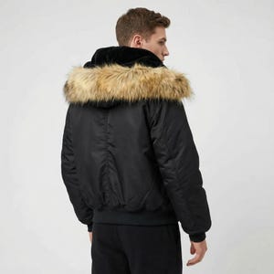 K&ouml;nnte beinhalten: Schwarze Bomberjacke mit Kapuze mit Kunstfellbesatz. Die Jacke hat einen gerippten Saum und B&uuml;ndchen. Das Model tr&auml;gt eine schwarze Hose. Die Kapuze der Jacke ist mit schwarzem Samt gef&uuml;ttert.
